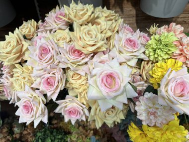 Pastel güller ve sarı kasımpatılar da dahil olmak üzere yapay çiçeklerin düzenlenmesi, dekoratif bir ortamda ayrıntılı taç yaprakları ve canlı renklerin vurgulanması