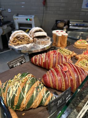 Fırın vitrininde cam raflarda sergilenen yeşil ve kırmızı kruvasanlar, tatlı ekmekler ve diğer fırınlanmış gıdalar dahil çeşitli hamur işleri.