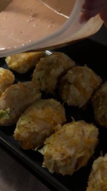 Sebzeli hamur köfteleri siyah bir kabın içine yerleştiriliyor ve üzerine sos dökülüyor.