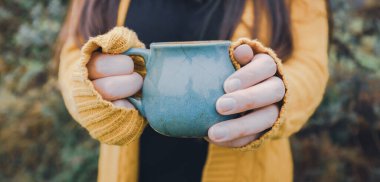 Young woman hands holding a blue mug of tea outdoor