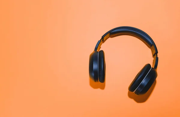 Black wireless headphones isolated on an orange background. — Stock Photo, Image