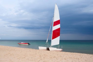 Kırmızı ve beyaz yelkenli güzel beyaz katamaran sahilde. Gökyüzü mavi bulutlu arka plan.