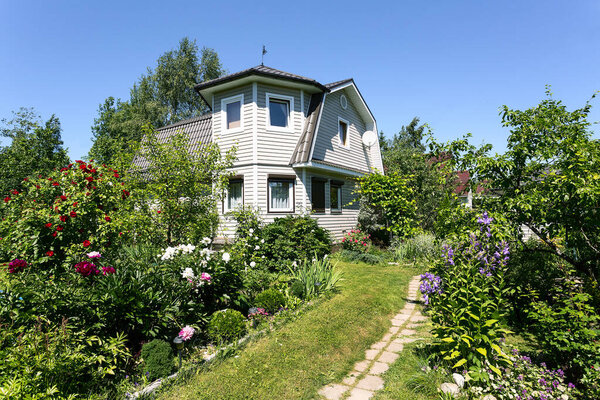 Country house with a siding sheathed metal roof surrounded by greenery in summer time in Russia. 