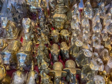 Pirinçten ya da benzer bir maddeden yapılmış küçük, parlak, metalik nesnelerden oluşan bir koleksiyon. Bu eşyalar, muhtemelen kültürel veya dini öneme sahip, kalabalık bir pazar veya mağaza vitrininde düzenlenmiş dekoratif figürler veya hediyelik eşyalar gibi görünüyor..