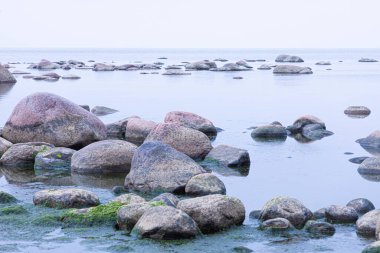 Canlı, renkli ve parlak bir arka plan, manzara. Deniz ya da okyanus kıyısında ya da nehir kıyısında, göl ya da kilosu sakin havalarda su yüzeyiyle kaplı brüt granit kaya ve taş manzarası veya görüntüsü