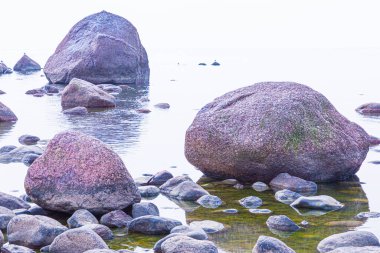 Canlı, renkli ve parlak bir arka plan, manzara. Deniz ya da okyanus kıyısında ya da nehir kıyısında, göl ya da kilosu sakin havalarda su yüzeyiyle kaplı brüt granit kaya ve taş manzarası veya görüntüsü