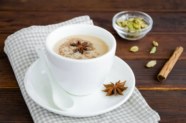 Hot tea with milk, cinnamon, cardamom, anise and other spices, Indian masala tea in a white cup on a wooden background. copy space