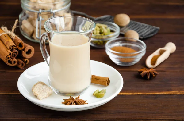 Hot tea with milk, cinnamon, cardamom, anise and other spices, Indian masala tea in a glass cup on a wooden background. copy space