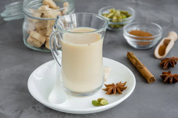 Hot tea with milk, cinnamon, cardamom, anise and other spices, Indian masala tea in a glass on a dark background. copy space