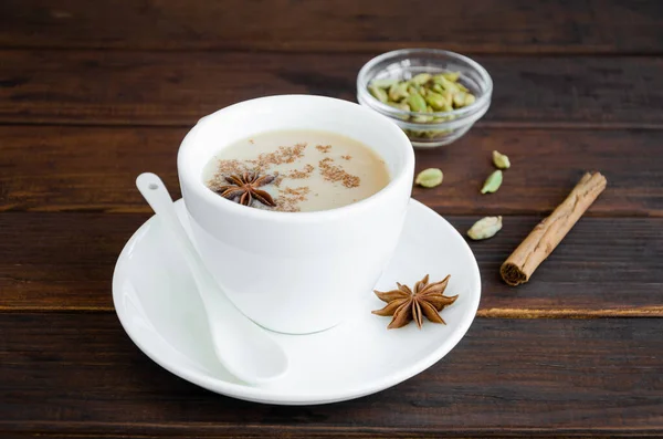 Hot tea with milk, cinnamon, cardamom, anise and other spices, Indian masala tea in a white cup on a wooden background. copy space