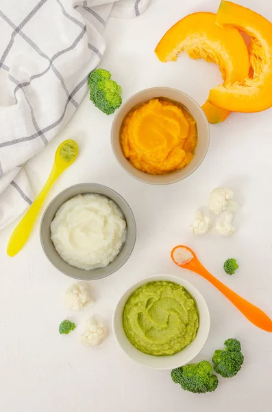 Baby food. Variation of the three homemade vegetable puree in bowls. Pumpkin puree, cauliflower puree and broccoli puree on a white background. Top view — Stock Image Baby Food Variation Three Homemade Vegetable Puree Bowls Pumpkin Puree Royalty Free Stock Images