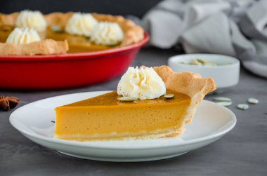 Geleneksel balkabağı turtası, baharatlar, krem şanti ve tohumlar koyu taşlı arka planda. Şükran Günü için tatlı.