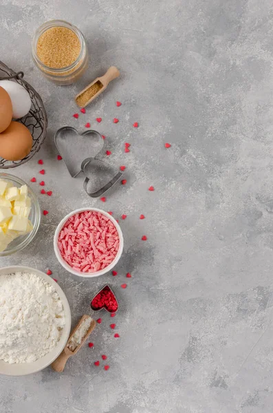 Ingredients for cooking cookies for Valentine\'s Day, flour, butter, eggs, sugar, chocolate and sugar hearts on a gray concrete background. Valentine\'s Day background. Copy space