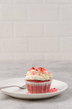 Krem peynirli kırmızı kadife kekler gri arka planda beyaz bir tabakta Sevgililer Günü için süslenir. Boşluğu kopyala