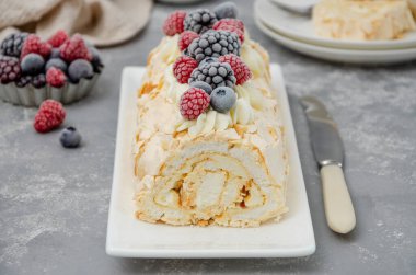 Meringue roll Pavlova cake with cream and raspberries, blackberries and blueberries on top on a gray background. Copy space clipart