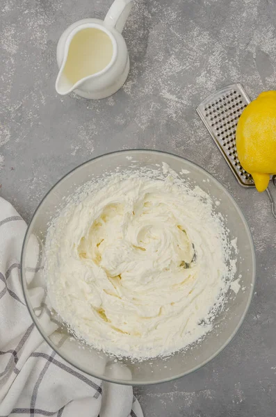 Cooking meringue Pavlova roll cake. ?ream for Pavlova cake of cream cheese, cream, sugar and lemon zest in a bowl on a gray concrete background. Recipe step by step. Vertical, Top view