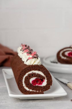 Krem şantili ve vişneli Black Forest çikolatalı kek rulosu gri bir arka planda. Boşluğu kopyala