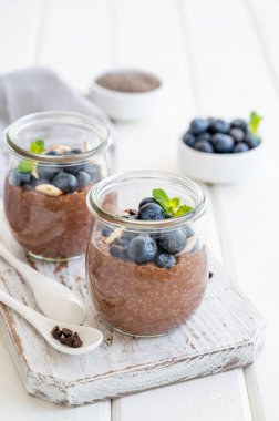 Yaban mersinli çikolatalı chia pudingi, badem ve nane şekeri beyaz ahşap arka planda cam bir kavanozda. Sağlıklı yiyecekler. Boşluğu kopyala