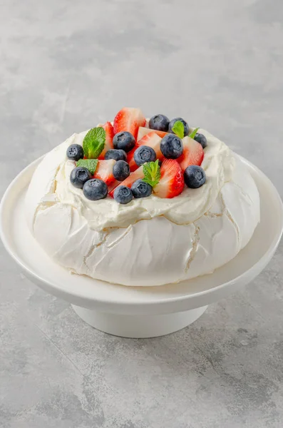 Pavlova meringue cake with whipped cream and fresh berries on top on a plate on a gray concrete background. Summer dessert. Copy space