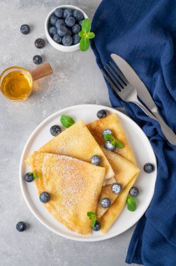 Taze yaban mersini ve toz şekerle servis edilen ev yapımı krepler gri beton arka planda beyaz bir tabakta. Maslenitsa için yemek. Boşluğu kopyala