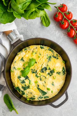 Ispanaklı omlet, yeşil soğan ve gri beton arka planda dökme demir tavada feta peyniri. Sağlıklı kahvaltı. Üst görünüm, alanı kopyala