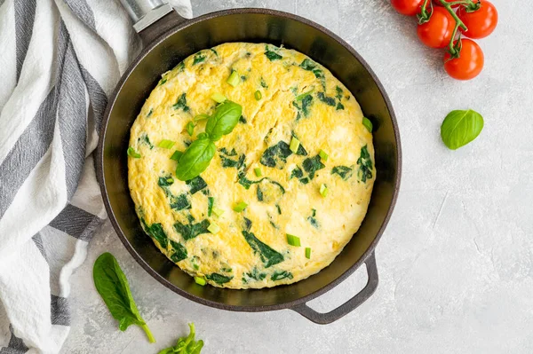 Ispanaklı omlet, yeşil soğan ve gri beton arka planda dökme demir tavada feta peyniri. Sağlıklı kahvaltı. Üst görünüm, alanı kopyala