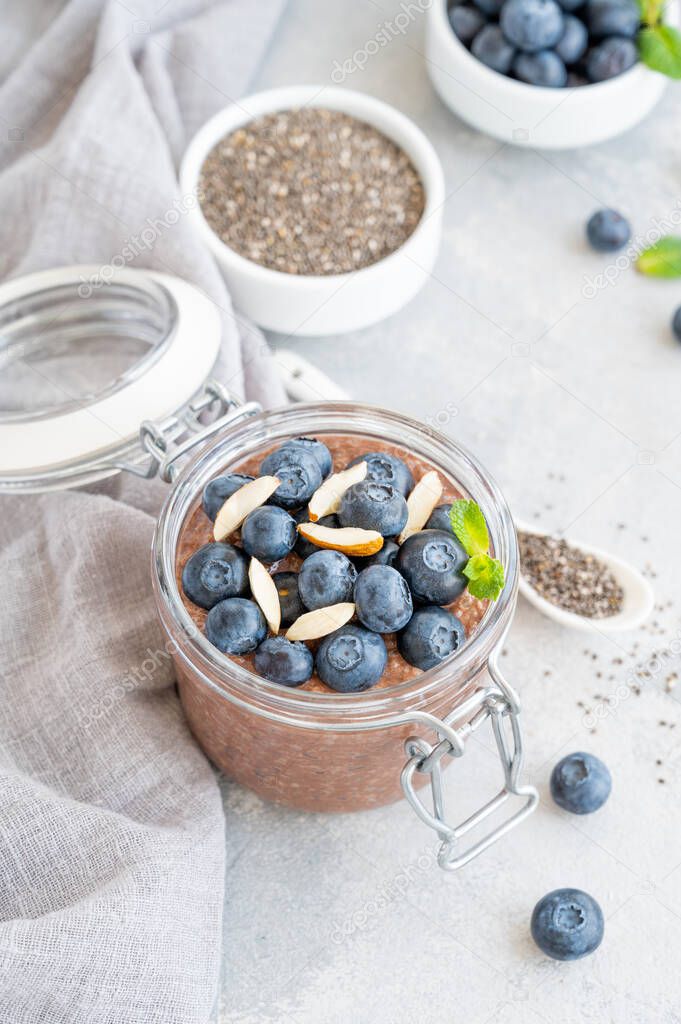 Chocolate chia pudding with blueberry, almonds and mint on top in a glass jar on a gray concrete background. Healthy food. Copy space