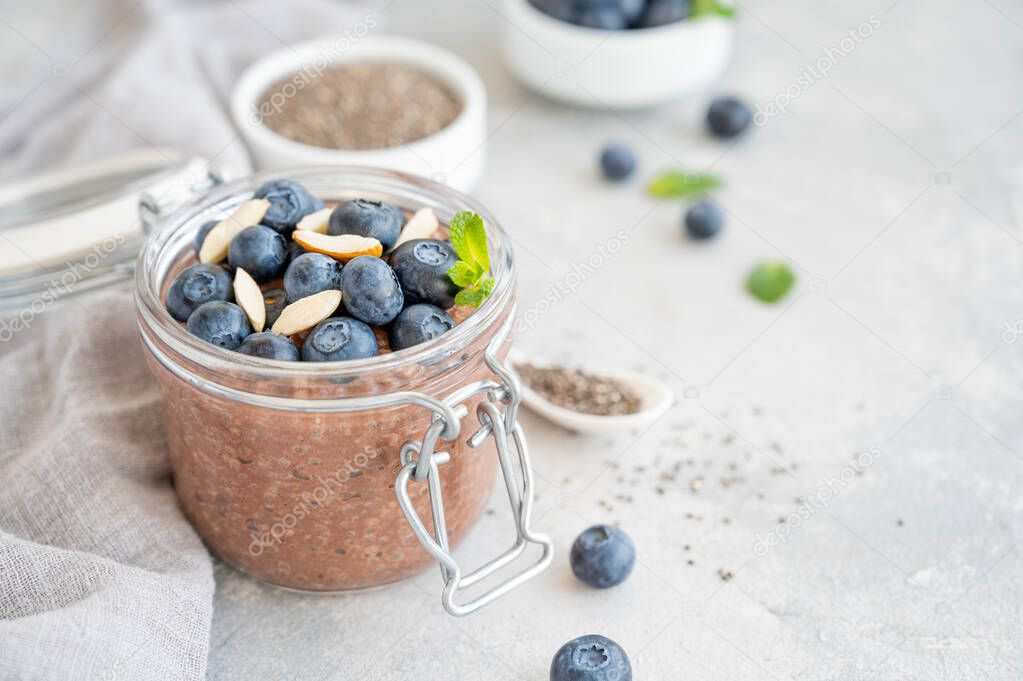 Chocolate chia pudding with blueberry, almonds and mint on top in a glass jar on a gray concrete background. Healthy food. Copy space