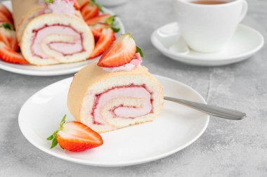 Taze çilek, reçel ve krem peynirli kek rulosu gri arka planda beyaz bir tabakta. Boşluğu kopyala