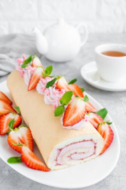 Taze çilek, reçel ve krem peynirli kek rulosu gri arka planda beyaz bir tabakta. Boşluğu kopyala