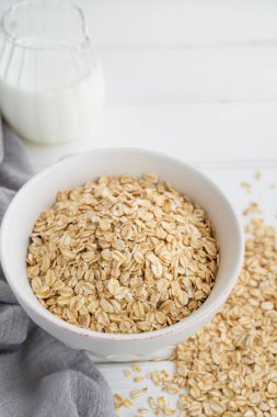 Beyaz ahşap arka planda sütlü bir kasede çiğ yulaf ezmesi. Sağlıklı yiyecekler. Boşluğu kopyala