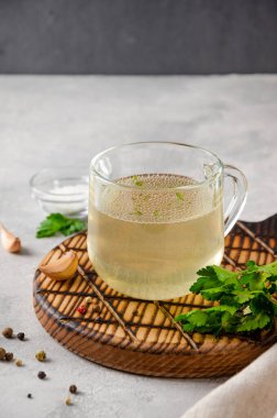 Cam bardakta tavuk suyu, maydanoz, sarımsak ve diğer baharatlar gri beton arka planda tahta bir tahtada. Boşluğu kopyala