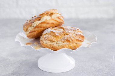 Geleneksel Fransız pastası Paris Brest, kremalı, pudra şekerli ve gri beton arka planda badem yapraklı. Boşluğu kopyala