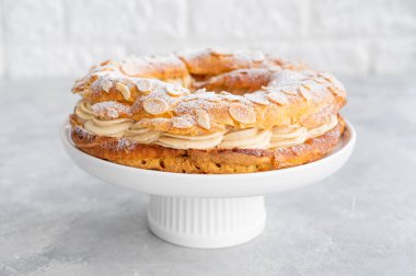 Geleneksel Fransız pastası Paris Brest, kremalı, pudra şekerli ve gri beton arka planda badem yapraklı. Boşluğu kopyala