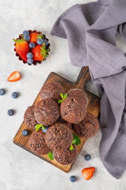 Çikolatalı kek ya da üzerinde çikolata damlaları olan kapkekler gri arka planda, üzerinde taze böğürtlen ve nane olan tahta bir tahta tahta üzerinde. Boşluğu kopyala