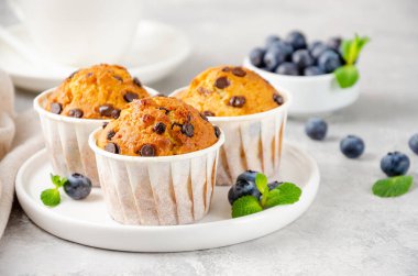 Beyaz tabakta çikolatalı kekler, bir fincan kahve ve gri beton arka planda taze yaban mersini. Boşluğu kopyala