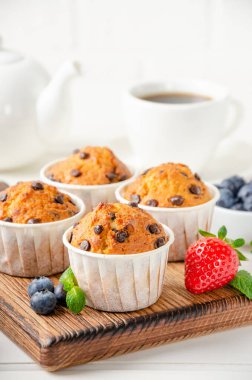 Beyaz arka planda, üzerinde çikolata parçacıkları olan muffinler ve taze böğürtlenler. Boşluğu kopyala