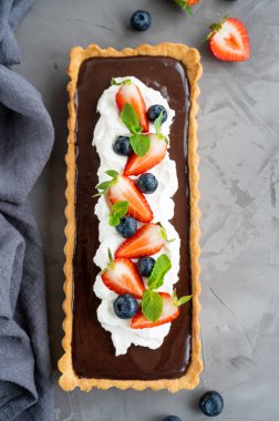 Krem şantili çikolatalı tart, koyu arkaplanda taze yaban mersini ve çilek. Yaz tatlısı