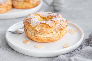 Geleneksel Fransız pastası Paris Brest, kremalı, pudra şekerli ve gri beton arka planda badem yapraklı. Boşluğu kopyala