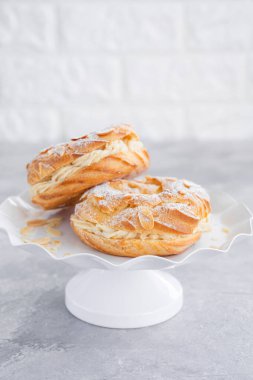 Geleneksel Fransız pastası Paris Brest, kremalı, pudra şekerli ve gri beton arka planda badem yapraklı. Boşluğu kopyala