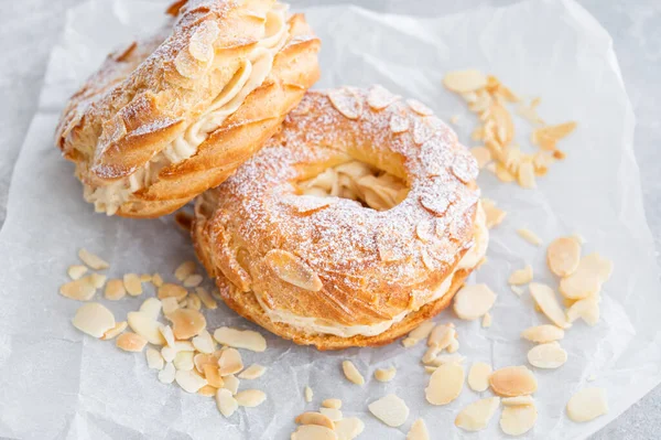 Geleneksel Fransız pastası Paris Brest, kremalı, pudra şekerli ve gri beton arka planda badem yapraklı. Boşluğu kopyala
