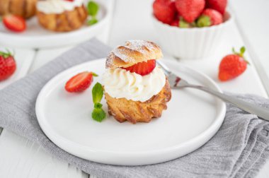 Lezzetli ev yapımı küçük kekler kremalı profiterol choux pastası, beyaz ahşap arka planda çilek ve krema tozu. Boşluğu kopyala