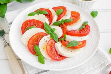 Klasik mozarella peynirli caprese salatası, domates ve fesleğen beyaz bir tabakta ahşap arka planda. Üst görünüm, alanı kopyala