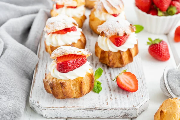 Lezzetli ev yapımı küçük kekler kremalı profiterol choux pastası, beyaz ahşap arka planda çilek ve krema tozu. Boşluğu kopyala