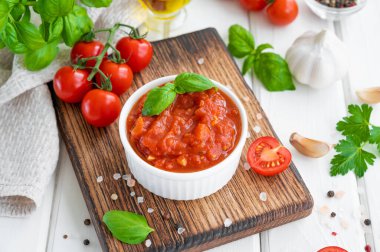 Geleneksel İtalyan marinara sosu beyaz ahşap arka planda baharat ve malzemelerle dolu bir kasede. Boşluğu kopyala