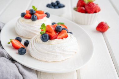 Krem şantili Pavlova kremalı pasta ve beyaz ahşap arka planda bir tabağın üstünde taze böğürtlen. Yaz tatlısı. Boşluğu kopyala