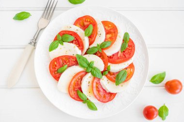 Klasik mozarella peynirli caprese salatası, domates ve fesleğen beyaz bir tabakta ahşap arka planda. Üst görünüm, alanı kopyala