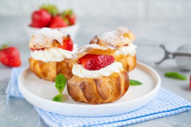 Lezzetli ev yapımı küçük kekler muhallebi, çilek ve gri beton arka planda krema tozlu profiterol choux hamur işi. Boşluğu kopyala