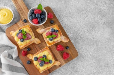 Krema ve taze böğürtlenli Danimarka puf kekleri, beton bir arka planda tahta bir tahtaya pudra şekeri serpiştirilmiş. Üst görünüm, alanı kopyala