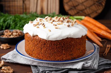 Carrot cake with cinnamon, walnuts and cream cheese frosting on a plate on a dark wooden background. Rustic style. Copy space